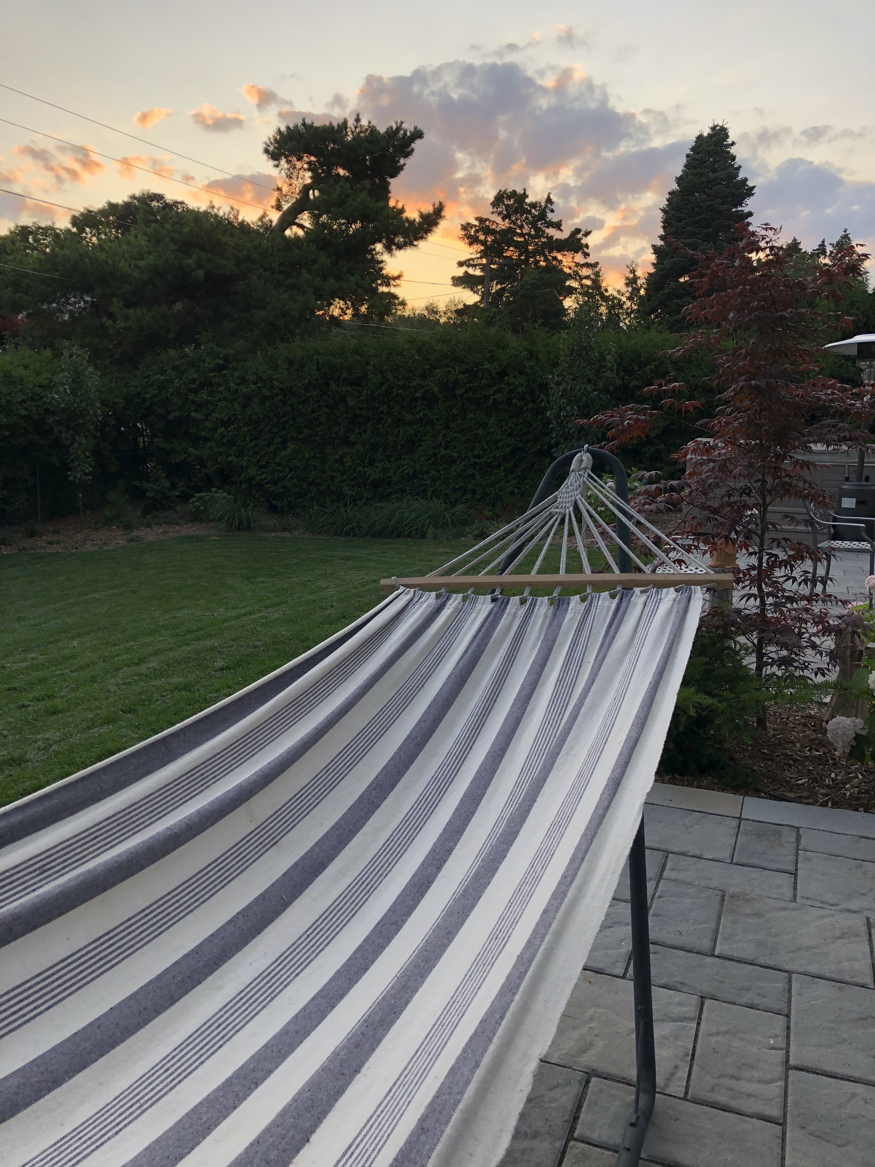 The sun sets over a striped hammock in a backyard